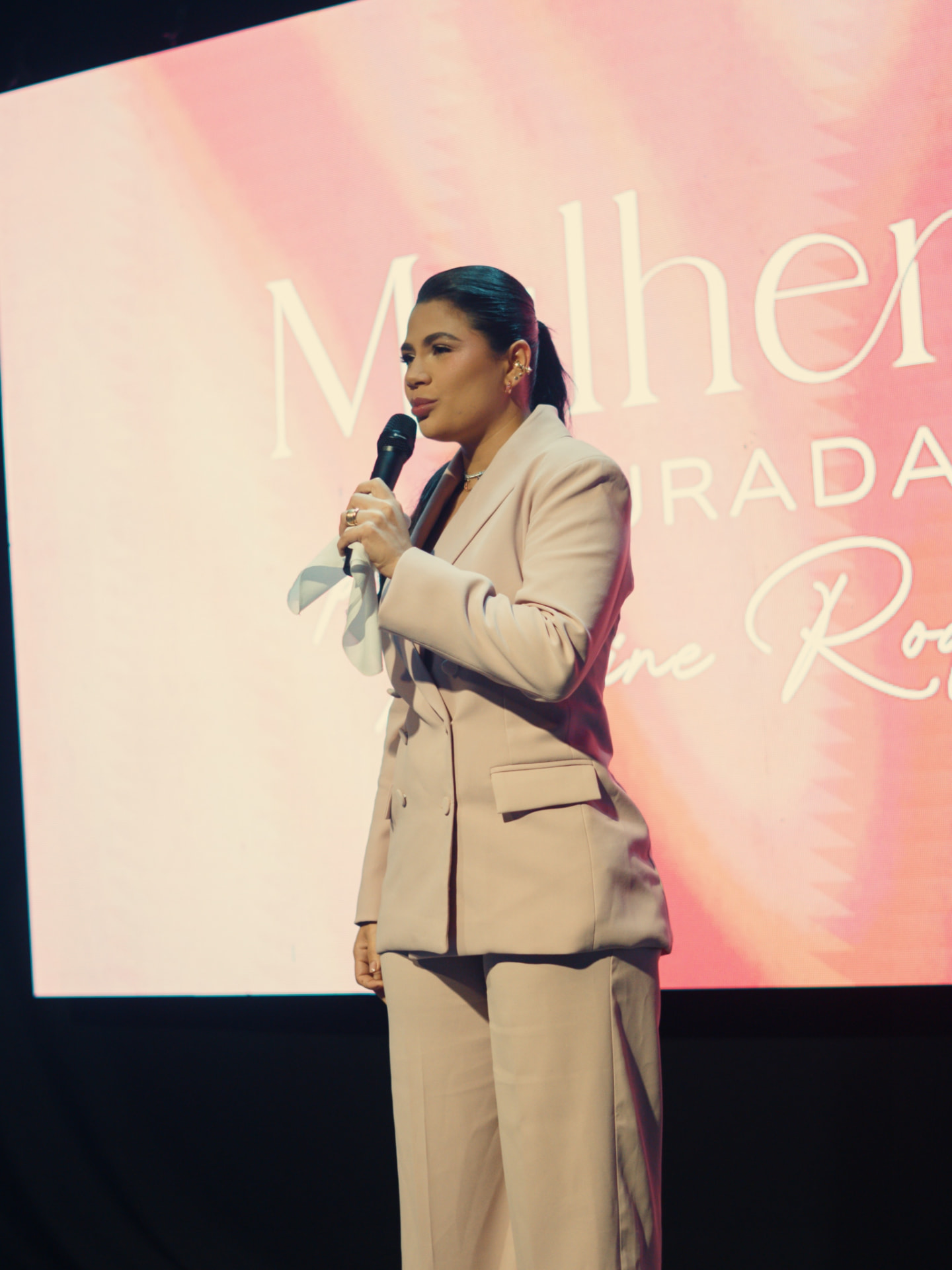 Palestrante ao microfone diante do painel Mulheres Curadas