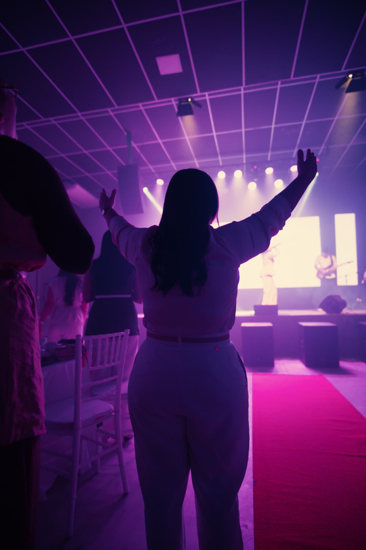 Participante de braços erguidos em adoração diante do palco