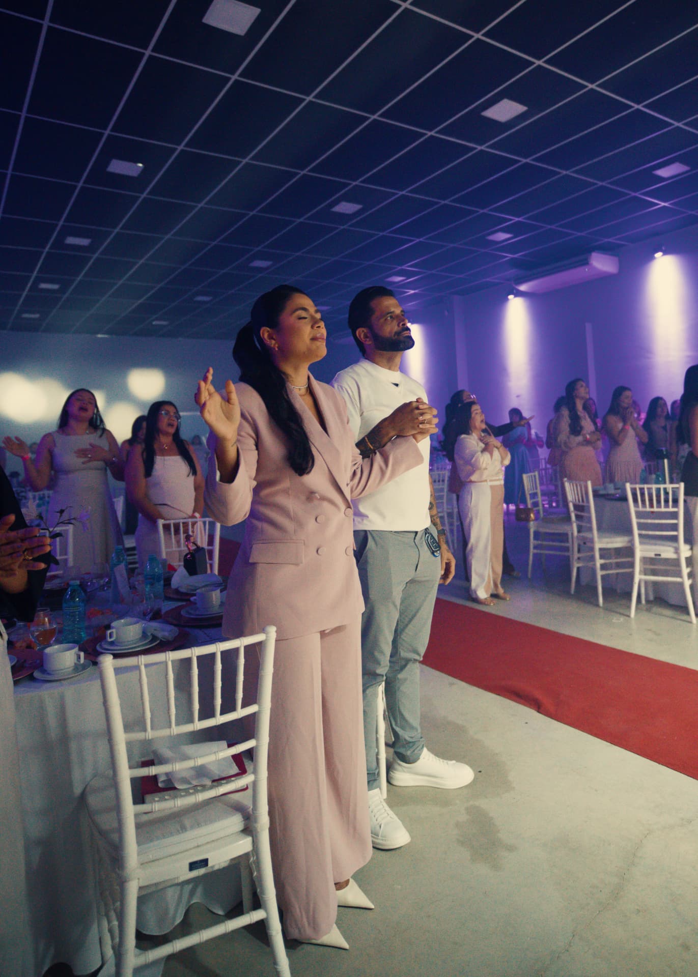 Participantes de pé, cantando juntas no salão do encontro